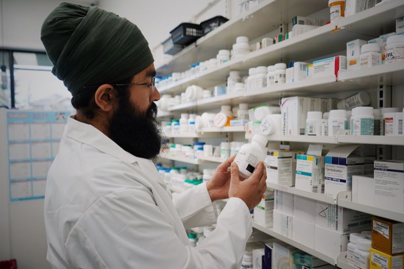 Apotheker prüft eine Packung vor dem Medikamentenregal